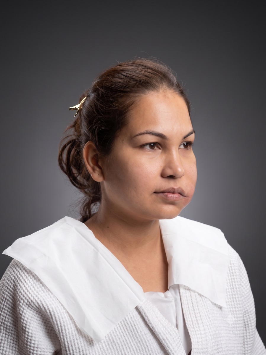 Client before her appointment, bare skin in a salon cape against a plain studio backdrop