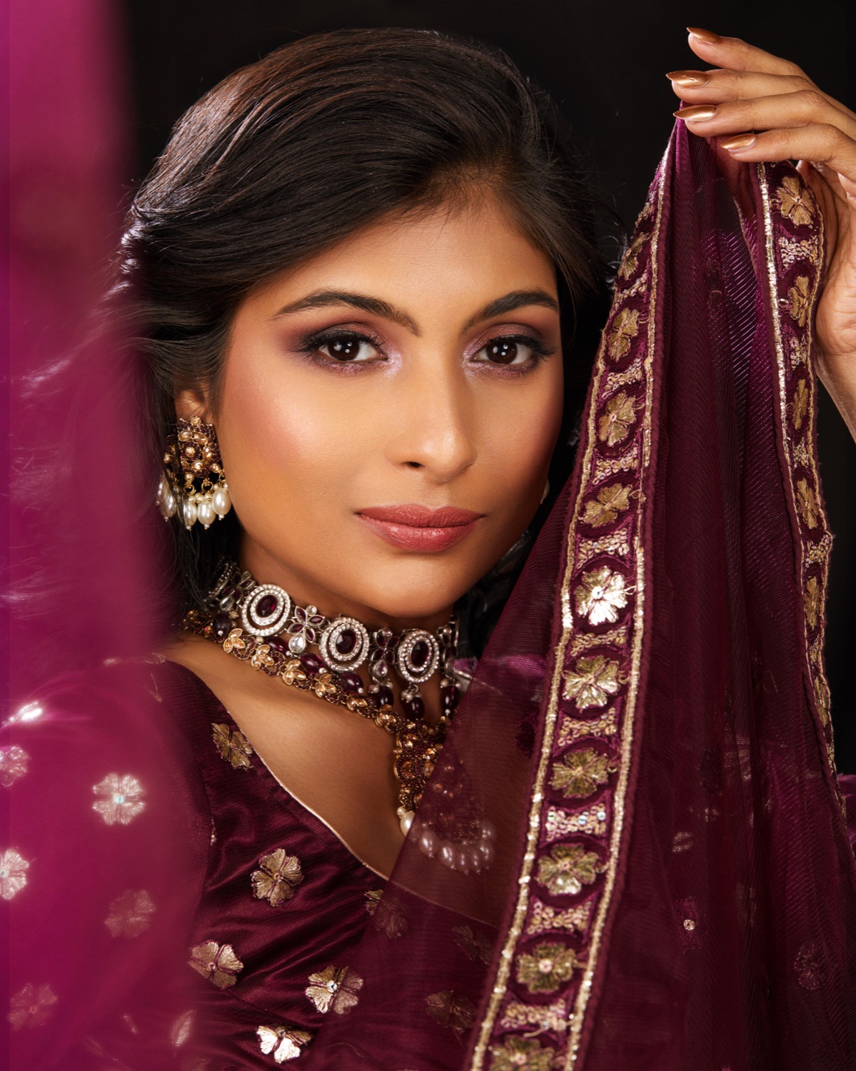 Bride in a deep maroon embroidered dupatta with warm skin-first makeup and gold jewellery